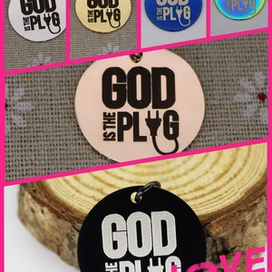 May include: A set of round metal charms with the phrase "God is the Plug" in black lettering. The charms are available in silver, gold, rose gold, blue, and rainbow colors.