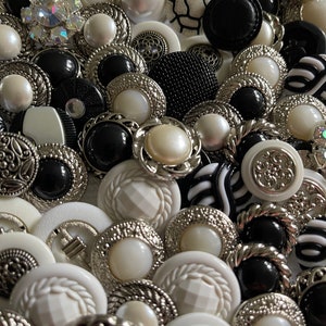 May include: A collection of black and white buttons with various designs and textures. Some buttons have a silver finish, while others have a pearl-like finish.