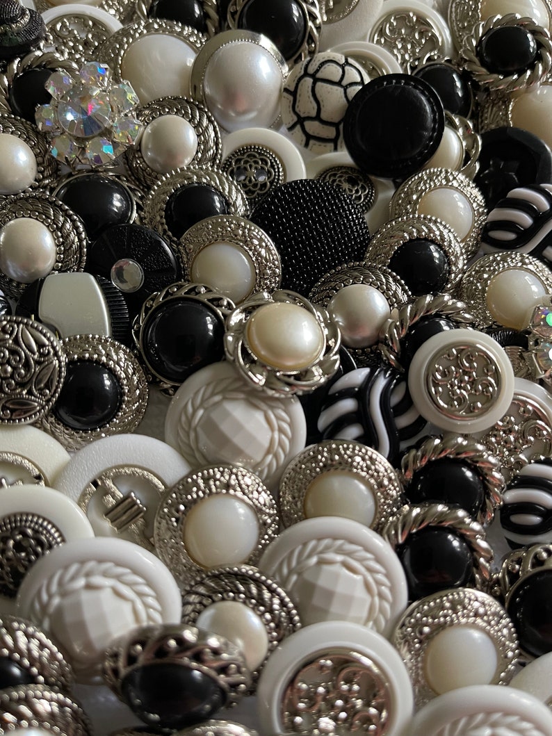May include: A collection of black and white buttons with various designs and textures. Some buttons have a silver finish, while others have a pearl-like finish.