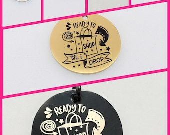 May include: A set of round metal keychains with a black and white design featuring a shopping bag and the text "Ready to Shop 'til I Drop". The keychains are available in gold, silver, black, and blue.