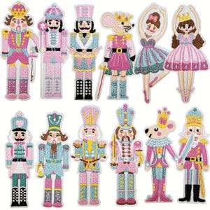 Könnte beinhalten: Eine Sammlung von zwölf gestickten Aufnähern mit Nussknacker-Figuren, einem Mäusekönig und Balletttänzern. Die Designs zeigen verschiedene Charaktere in rosa, blauen und goldenen Uniformen, die Schwerter oder Instrumente halten, mit detaillierten Stichen.