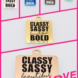 Può includere: Cinque ciondoli quadrati dorati, argentati, blu e iridescenti con il testo "Classy Sassy beautiful BOLD Zeta Phi Beta" stampato in nero. Un sesto ciondolo dorato con lo stesso testo è mostrato con un cuore rosa e il testo "Love Story" stampato in nero.