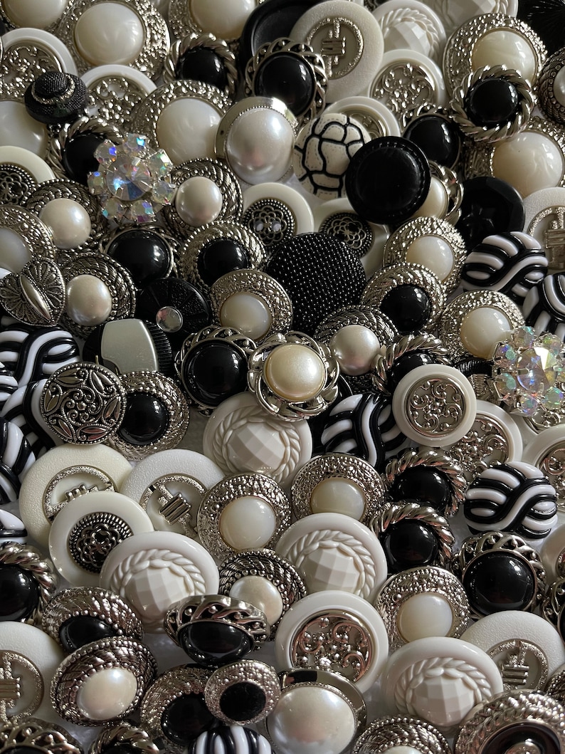 May include: A collection of black and white buttons with various designs and textures. The buttons are made of different materials, including plastic, metal, and fabric. Some buttons have a shiny finish, while others have a matte finish.