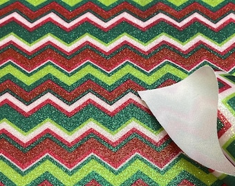 May include: Glittery Christmas-themed paper with a chevron pattern. The design features alternating bands of red, green, and white glitter, creating a festive and textured appearance. A corner of the paper is peeled back, revealing a white backing.