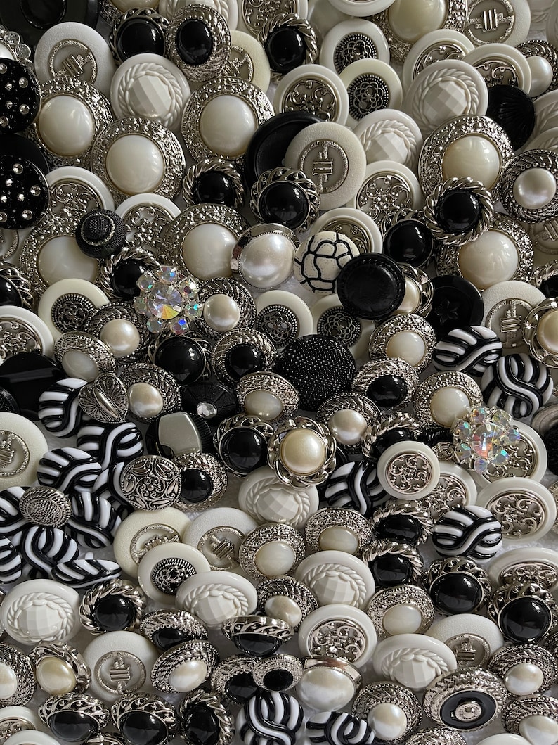 May include: A collection of black and white buttons with various designs and textures. The buttons are made of plastic, metal, and pearl. Some buttons have a silver finish, while others have a black or white finish.