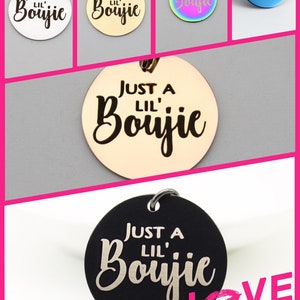 May include: A collection of round pendants in various colors, including silver, gold, iridescent, and blue. Each pendant features the phrase "JUST A LIL' Boujie" in a stylish script font. The pendants are designed with a small loop for attachment.