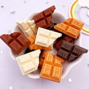 May include: A white bowl filled with various chocolate bar charms. The charms are in different colors, including brown, white, and orange. Each charm has the word "MILK" printed on it.