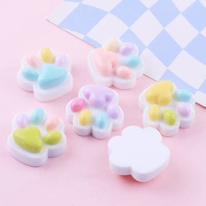 May include: Six pastel-colored resin paw print charms with white borders. The charms are in various colors, including pink, blue, yellow, and green.