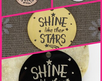May include: Four round metal charms with the text "Shine like the stars" in black lettering. The charms are in gold, silver, black, and rose gold.