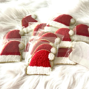 May include: A collection of small, red Santa hats with white trim and gold edging, packaged in clear plastic. The hats have a fluffy texture and a white pom-pom. Christmas-themed decorations.