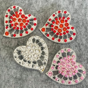 May include: Four heart-shaped decorative embellishments with silver metal frames and colorful rhinestones. Two hearts feature red rhinestones, one heart features clear rhinestones, and one heart features pink rhinestones.