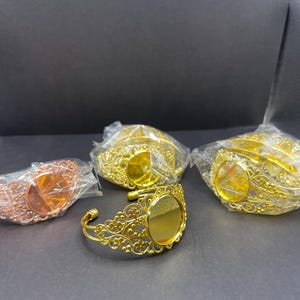 May include: Four gold-toned metal bracelets with a round, clear glass insert. The bracelets are in various stages of packaging.