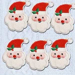 May include: Six embroidered Santa Claus patches. Each patch features a red hat with a white pom-pom, a white beard, rosy cheeks, a red nose, and a small sprig of green holly. The patches are on a light blue, textured background.