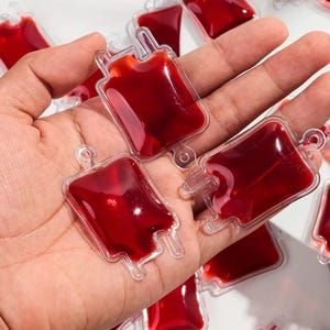 Peut inclure: Des breloques en forme de poche de sang en plastique transparent remplies d'un liquide rouge foncé. Les breloques ont une forme rectangulaire avec une boucle en haut pour les attacher à un porte-clés ou à un autre projet d'artisanat. Idéal pour Halloween.