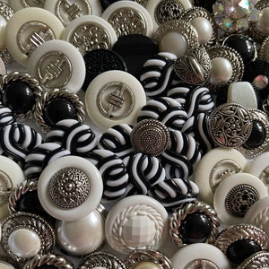 May include: A collection of black and white buttons with silver accents. The buttons are various shapes and sizes, including round, square, and oval. Some buttons have intricate designs, while others are plain.