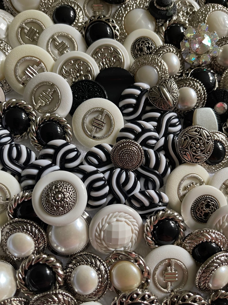May include: A collection of black and white buttons with silver accents. The buttons are various shapes and sizes, including round, square, and oval. Some buttons have intricate designs, while others are plain.
