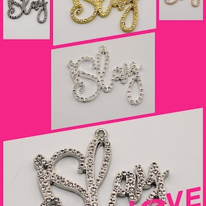 Op de afbeelding: Een zilveren bedel met het woord "Slay" gespeld in strass. De bedel is op een witte achtergrond met de tekst "Love Story" in zwart.