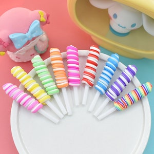 May include: A set of ten colorful swirl candy lollipops on white sticks. The lollipops are arranged in a semi-circle on a white plate. The lollipops are in the following colors: pink, yellow, green, orange, red, blue, purple, and rainbow.