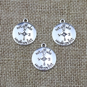 May include: Three silver charm pendants with a compass design and the text "not all who wander are lost".