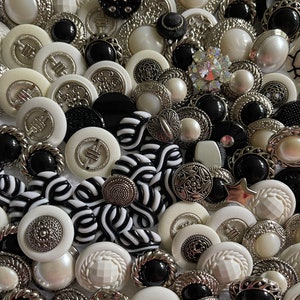 May include: A collection of black, white, and silver buttons with various designs and textures. The buttons are arranged in a random pattern and are all different sizes.