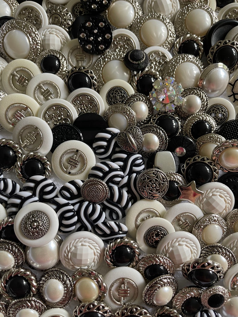 May include: A collection of black, white, and silver buttons with various designs and textures. The buttons are arranged in a random pattern and are all different sizes.