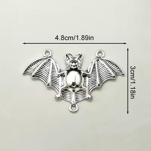 May include: A silver-toned metal bat charm featuring three circular attachment loops. The bat has detailed wing textures and a central body. Dimensions are clearly marked as 4.8cm wide by 3cm tall, with imperial equivalents of 1.89 inches by 1.18 inches.