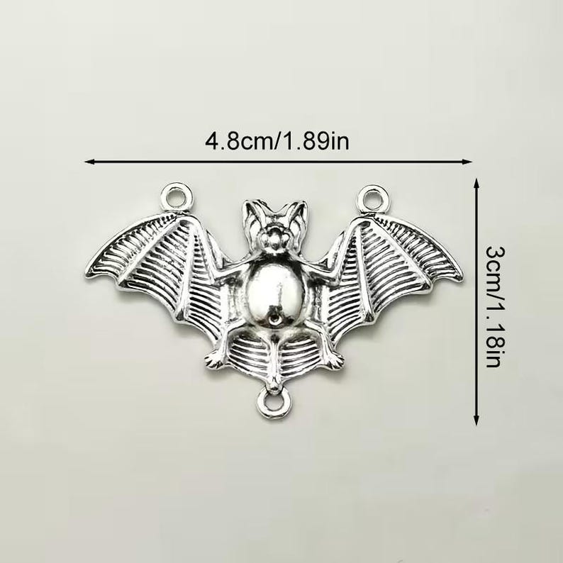 May include: A silver-toned metal bat charm featuring three circular attachment loops. The bat has detailed wing textures and a central body. Dimensions are clearly marked as 4.8cm wide by 3cm tall, with imperial equivalents of 1.89 inches by 1.18 inches.