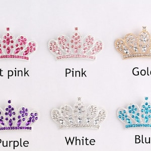 May include: Six silver crowns with different colored rhinestones. The crowns are arranged in two rows of three. The colors are hot pink, pink, gold, purple, white, and blue.