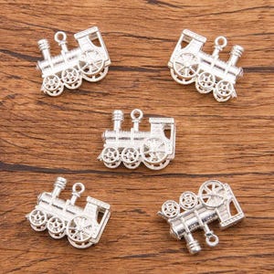 May include: Five silver-toned metal train charms with intricate details. Each charm features a locomotive with wheels, a smokestack, and a bell.