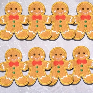 May include: Eight gingerbread man patches with smiling faces, red bow ties, and green buttons. The patches are tan with yellow outlines and white icing details. Ideal for festive crafts and seasonal projects.