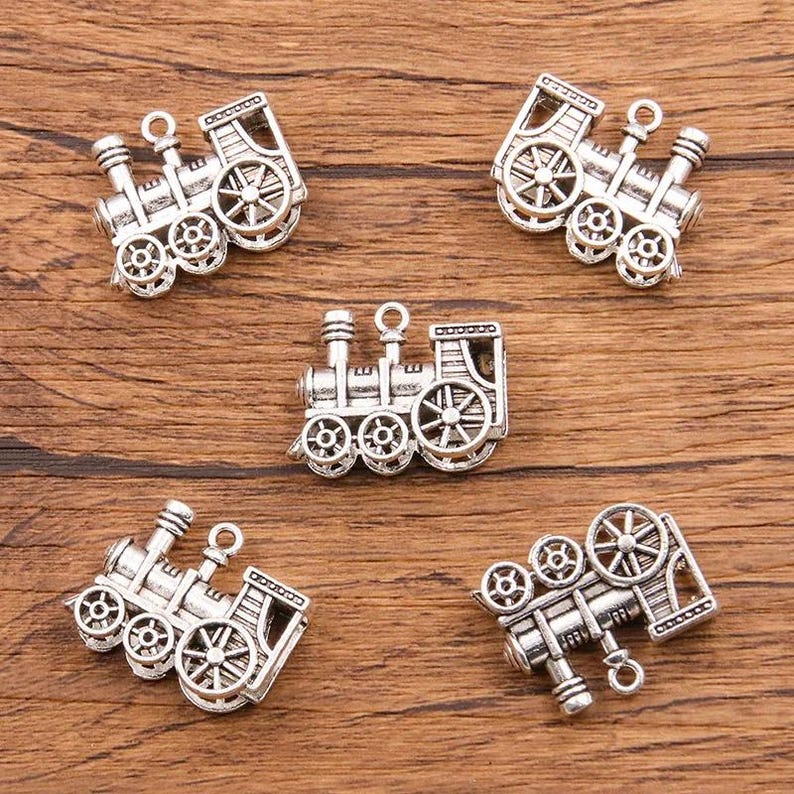 May include: Five silver-toned train charm pendants. Each charm features a detailed design of a locomotive with wheels, a smokestack, and a bell. The charms are perfect for adding a whimsical touch to jewelry or crafts.