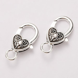 May include: Two silver-toned heart-shaped clasps with intricate floral designs. The clasps are designed for jewelry making and have a spring-loaded mechanism.