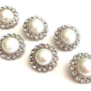 May include: Six round, silver-toned buttons with a large, pearlescent white center and a ring of clear, sparkling rhinestones around the edge. The buttons are arranged on a white background.