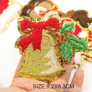 Puede incluir: Un parche de campana navideña dorada con purpurina, un lazo rojo y hojas verdes de acebo. El parche mide 9,2 x 8,3 cm. La campana está bordada con hilo dorado y tiene un contorno blanco. Es una decoración festiva.