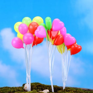 May include: A cluster of colorful heart-shaped balloons in shades of pink, red, yellow, and green. The balloons are tied together with clear string and are arranged in a semi-circle shape.