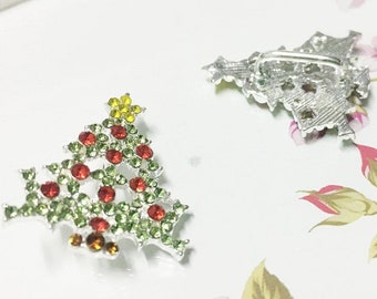 May include: Two silver Christmas tree brooches with red, green, and yellow rhinestones.