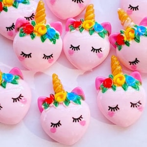 May include: Pink heart-shaped unicorn charms with a gold horn, closed eyes, and a floral crown with red, yellow, and blue flowers.