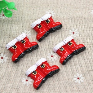 Puede incluir: Cuatro abalorios de botas de Papá Noel rojas y blancas con suelas negras. Las botas tienen un ribete de piel blanca y una hebilla dorada.