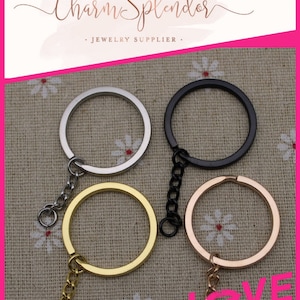 May include: Four key rings with chains in different colors: silver, black, gold, and rose gold. The key rings are on a fabric background with a floral pattern.