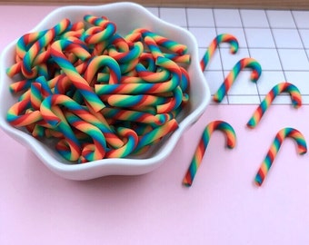 May include: A bowl filled with rainbow candy canes, with a few more candy canes scattered on a pink surface.