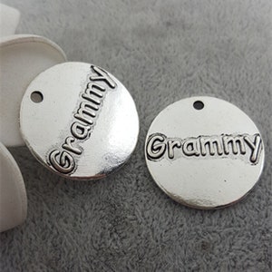 Puede incluir: Dos abalorios de metal plateados con la palabra "Grammy" en relieve. Los abalorios son redondos y tienen un agujero en la parte superior para sujetarlos a un collar o pulsera.