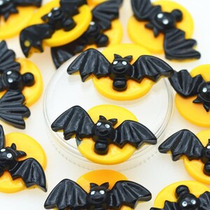 May include: A collection of black bat charms with yellow moon accents. The charms are made of plastic and have a glossy finish.