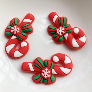 May include: Three red and white candy cane ornaments with green bows and a white snowflake on each. The ornaments are made of a soft, pliable material.