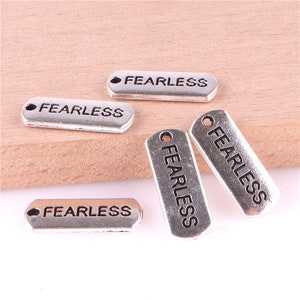 May include: Five silver-toned metal charms, each engraved with the word "FEARLESS". The charms are rectangular and have a small hole at the top for attaching to a necklace or bracelet.