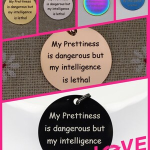 May include: Five round metal tags with the text "My Prettiness is dangerous but my intelligence is lethal" engraved on them. The tags are in different colors: gold, silver, rainbow, blue, and black. The black tag is on a white surface with the words "LOVE STORY" in pink letters.