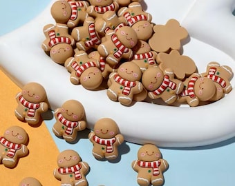 May include: A collection of gingerbread man-shaped ornaments with red and white striped scarves. Some are scattered on a light blue surface, while others are in a white, curved dish. The ornaments have smiling faces and are a light brown color.