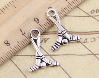 May include: Two silver-toned hockey stick charms with a small ball charm between the sticks. The charms are on a ruler with inch markings.