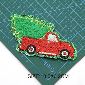 May include: Red pickup truck with a green Christmas tree in the bed. The truck and tree are embroidered with glitter. The image is on a green cutting mat with white markings. SIZE: 10.5X6.2CM
