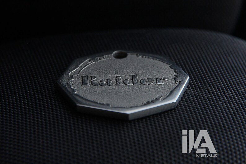 May include: A silver octagonal tag with the word "Raider" engraved on it.