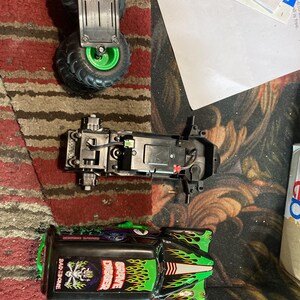 May include: A disassembled toy monster truck with green and black paint. The truck is labeled "Grave Digger" and "Bad to the Bone".